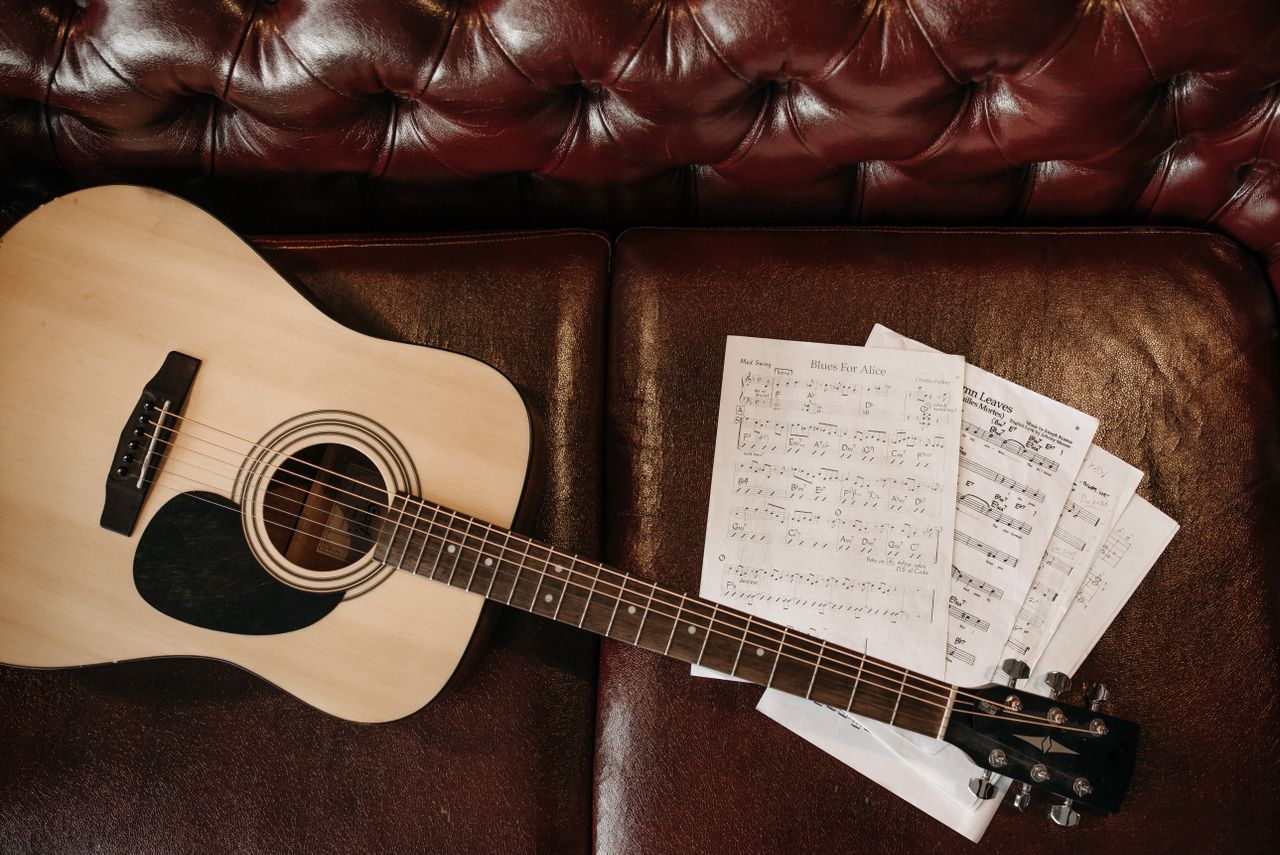 Home A flat lay of an acoustic guitar with sheet music on a leather sofa, perfect for music lovers.